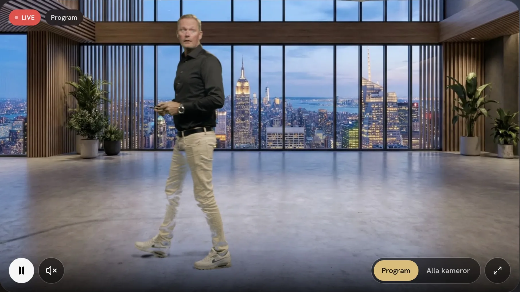 Programbilden live: en person som filmats mot green screen står i en virtuell kontorsmiljö med panoramafönster och stadsutsikt.